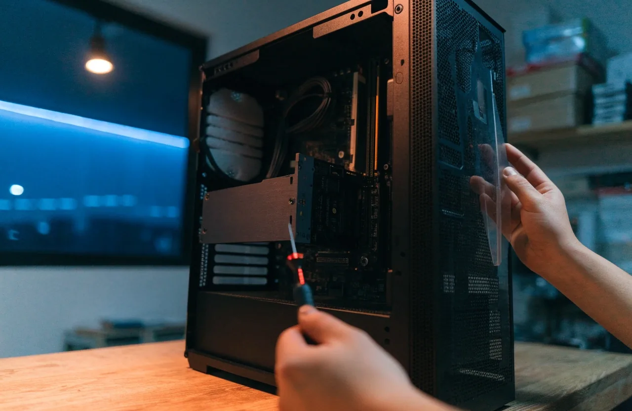 A graphics card being slid into a PCIe slot of an open desktop build on a work table under a lamp